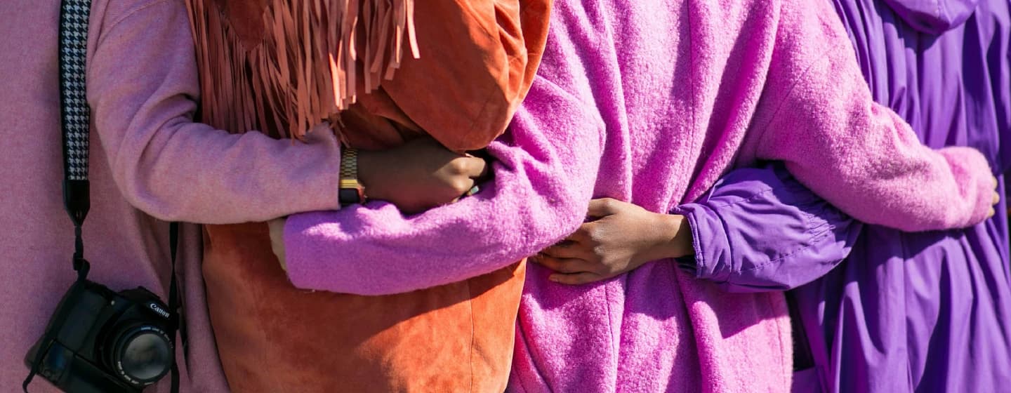 four bipoc women linking arms from behind representing unity