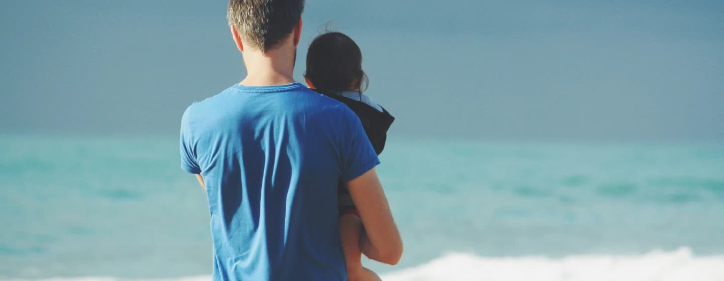 a millennial father holding his daughter looking out to see